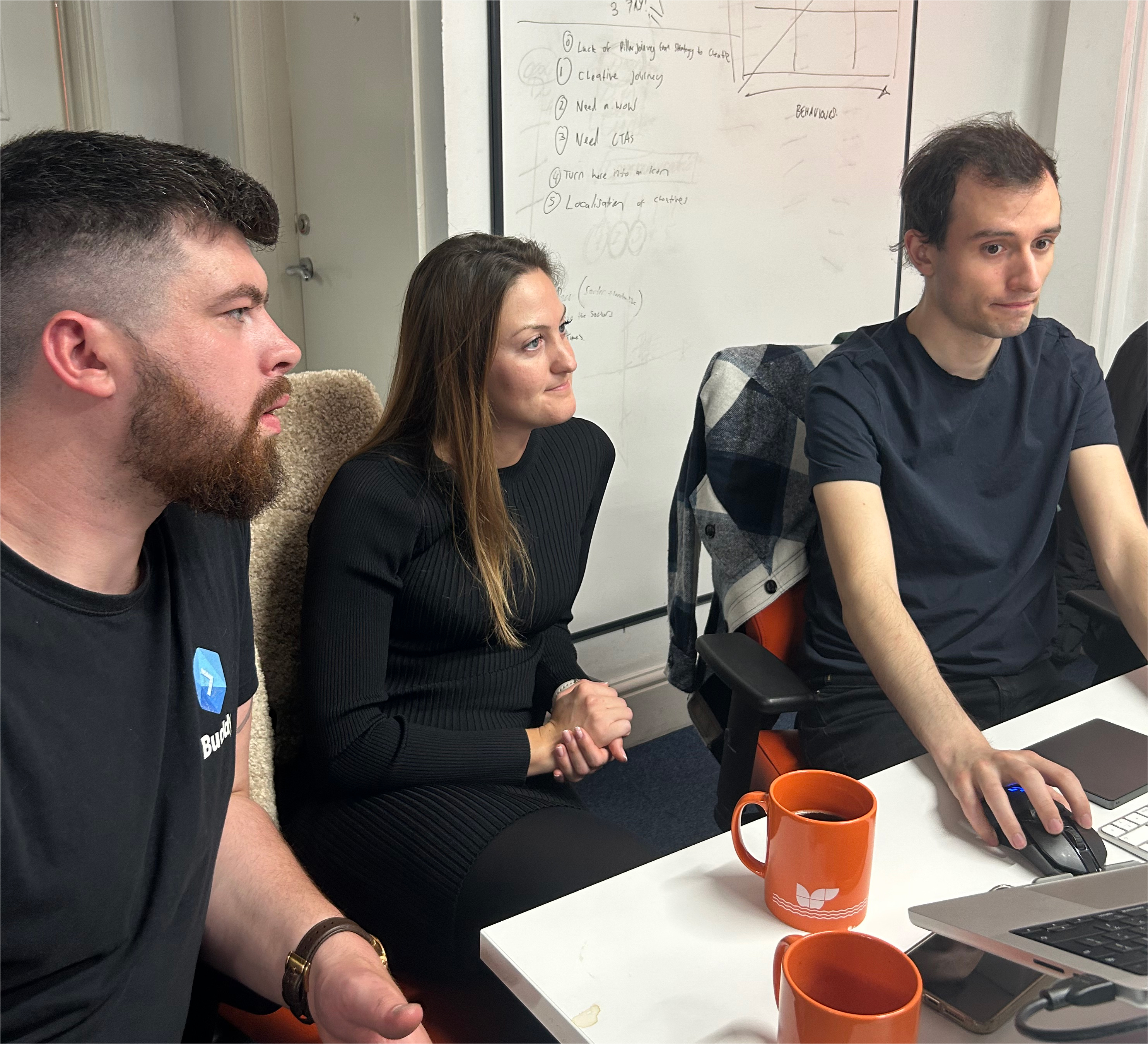 Three of Cyber-Duck's developers. They are sitting at a desk and discussing what they are working on, with cups of coffee on the desk in front of them.