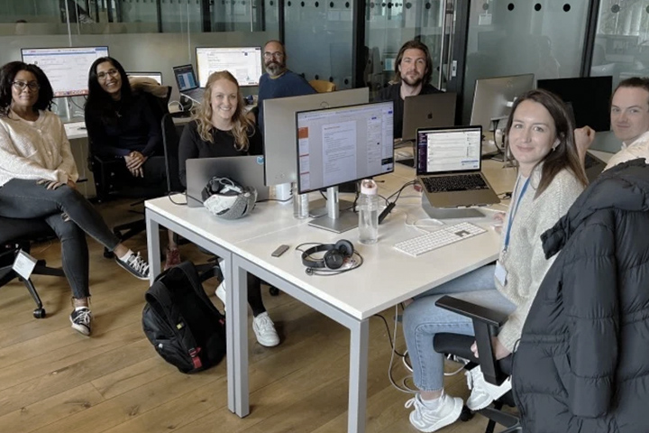 Seven members of Cyber-Duck seated at their desks in the office looking at the camera