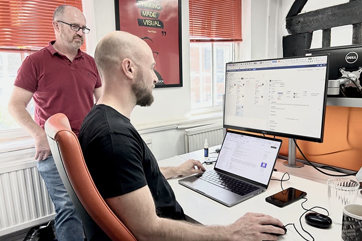 A technical architect and a front-end developer looking at two screens and discussing the software development process