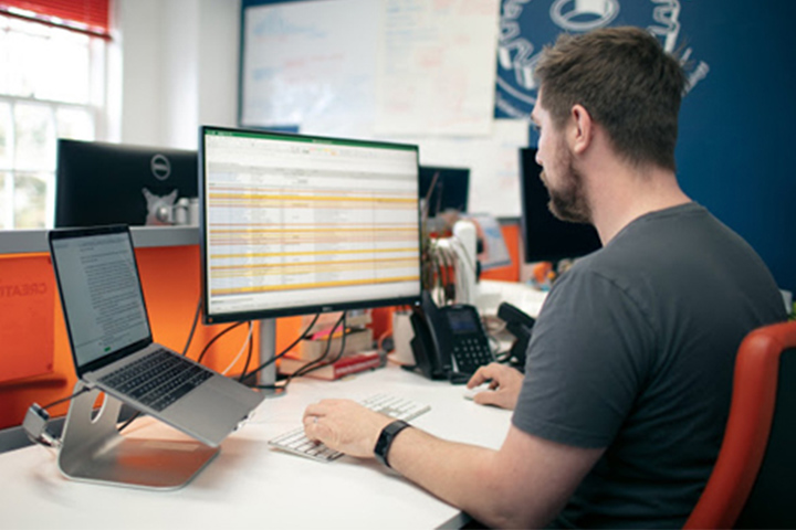 Photo of content design at his desk looking at data on an Excel spreadsheet