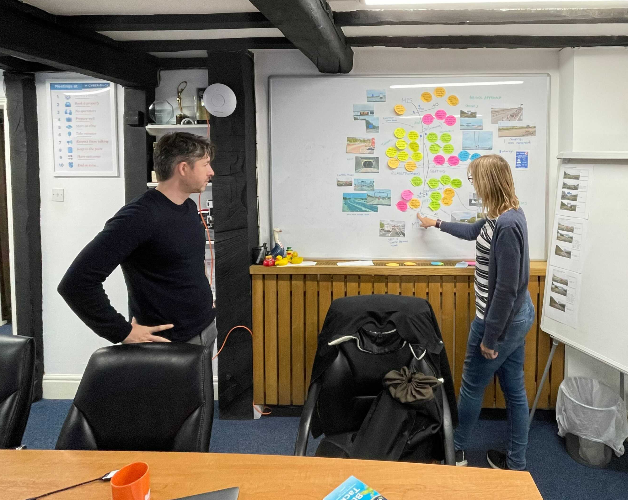 Two members of the Cyber-Duck team working on the strategy for National Highways, standing in front of a board covered with Post-It notes.