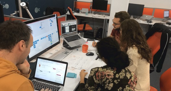 Group of people siting in front of two computers, talking