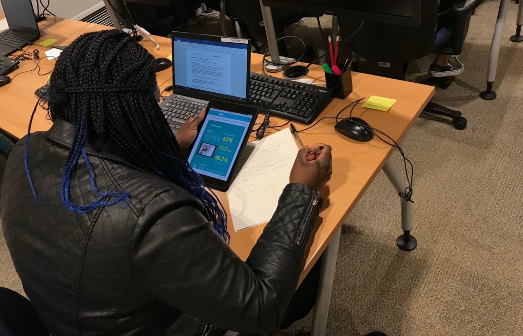FSAC partially digitised assesment process with a person with locs sitting at a desk working on a exercise with ipad and paper