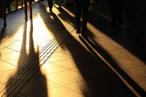 People casting shadows across the ground at sunset in the city