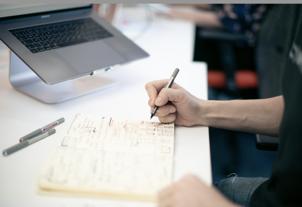 The hands of a designer, sketching out early ideas for user journeys and layouts in a notebook.