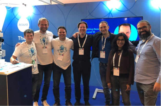 Group photo of three members of the Cyber-Duck team standing shoulder-to-shoulder alongside four members of the Acquia team at an Acquia exhibition stand