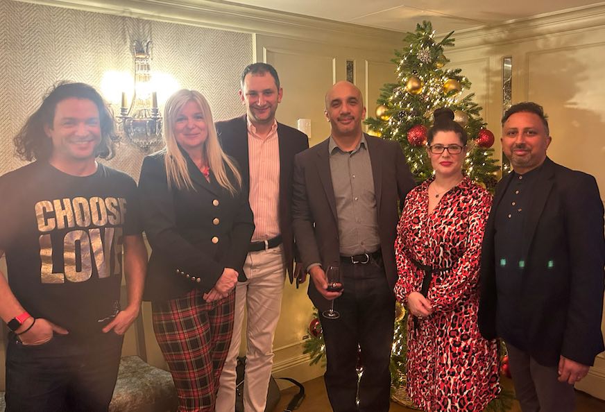 A photo of CEO Danny standing in a room with colleagues and clients for a photo in front of a Christmas tree