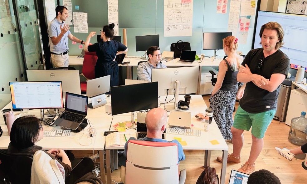 Slightly overhead shot of an office at Cyber-Duck resembling a hive of activity. Some staff are sitting at desks, others are standing.