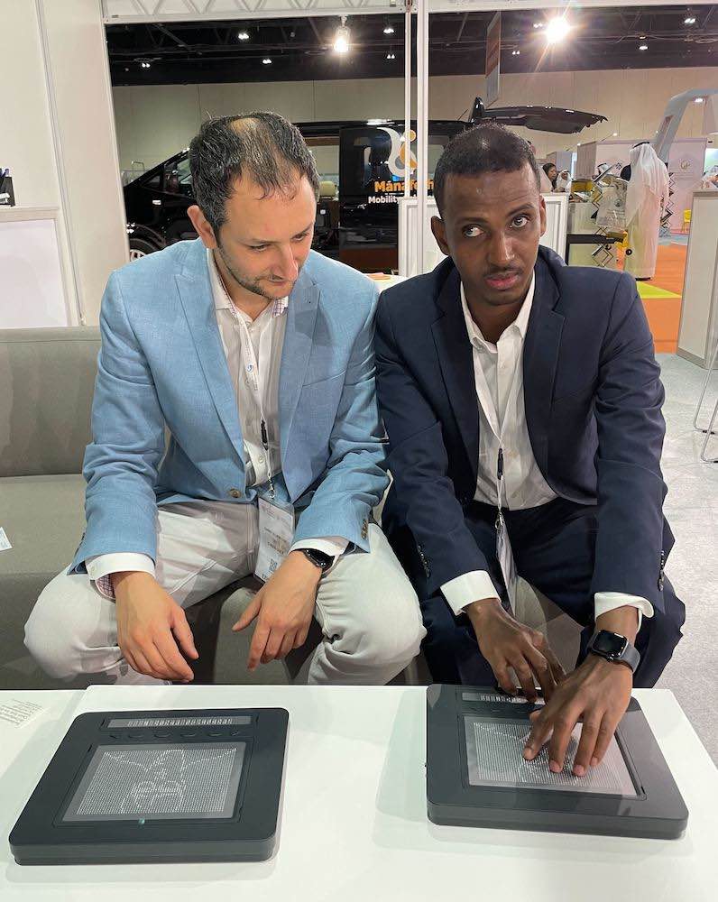 Photo of CEO Danny and accessibility consultant Yahye sitting at a table using a braille display