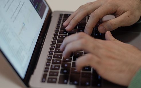 Close up photo of hands typing on a keyboard with a dev environment shown onscreen