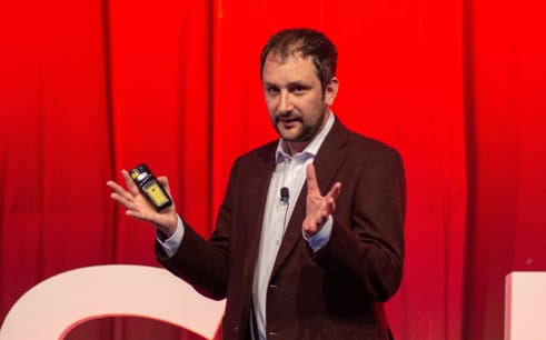Photo of CEO Danny giving a presentation in front of a bright red curtain