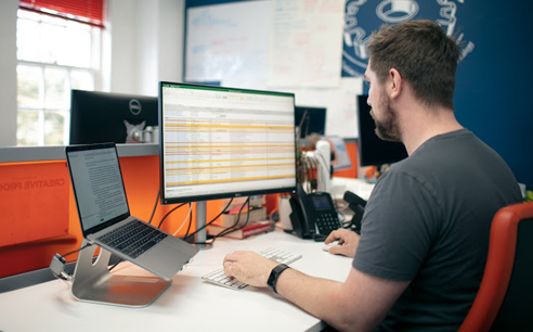 Photo of James at his desk looking at data on an Excel spreadsheet 