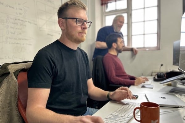 Photo of Gareth coding at his desk with two more Cyber-Duck devs behind him
