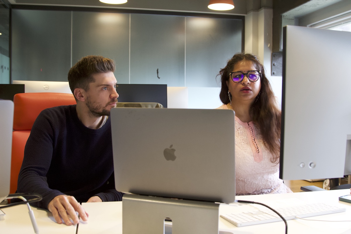 Two members of the digital optimisation team with laptops in front of them looking at a monitor at their desk