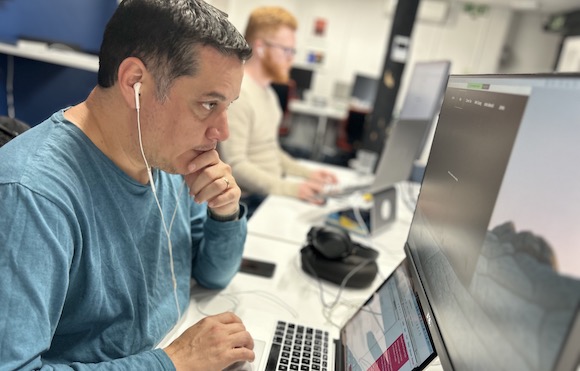 Photo of Tech Lead Ramon seated at his desk pondering over his office desktop monitor