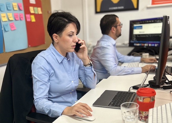 Photo of developer Alina speaking to a client on the phone at her desk whilst looking at her dev environment