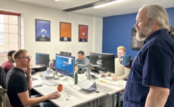 Photo of members of Cyber-Duck working at their desks in the office. Seated Gareth Drew is speaking to standing Gareth Alexander.